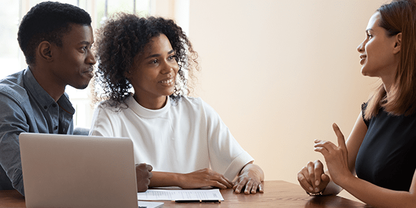 A couple having a discussion with a woman at a desk.