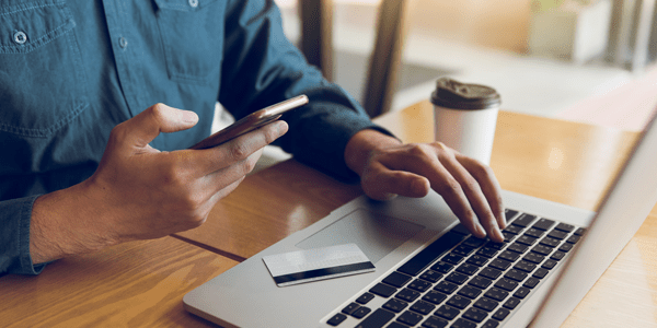 Hands of man holding smart phone and using laptop computer - l