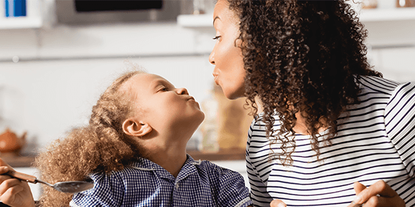 A woman and her daughter in a kitchen pouting at each other.