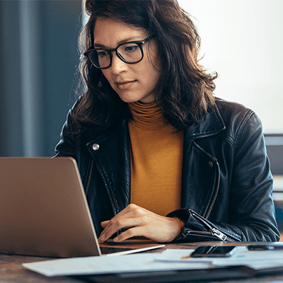 A woman with medium length curly brown hair typing on her laptop.