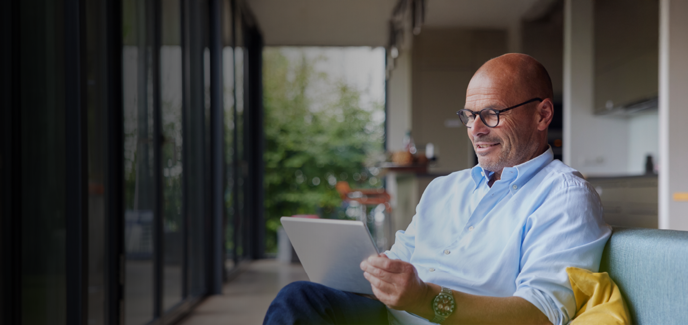 An older man smiling whilst sat on a sofa looking at his iPad.