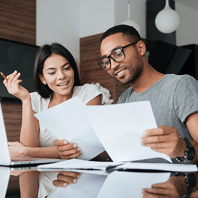 A man and woman smiling looking at papers on a desk discussing them.