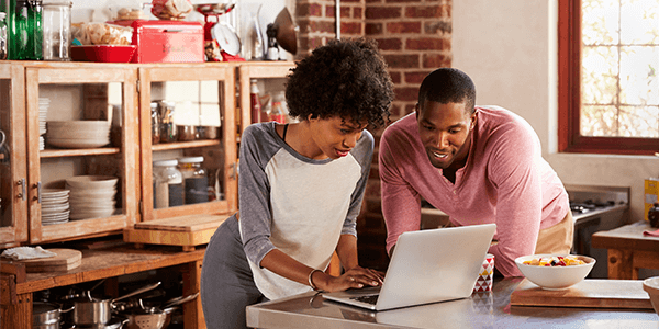 A couple stood up together looking at a laptop.