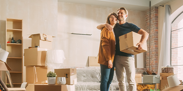 A couple with their arms around each other looking at a room filled with boxes.