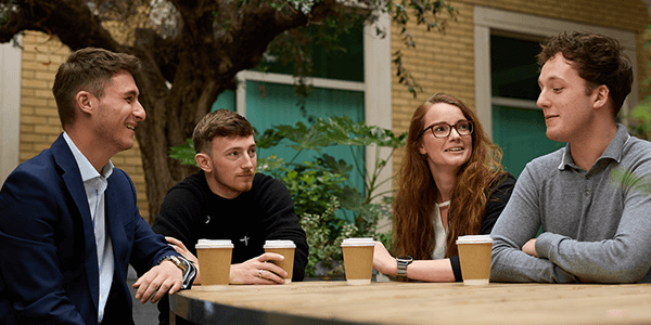 A group of colleagues sat at a table whilst drinking coffee and talking.