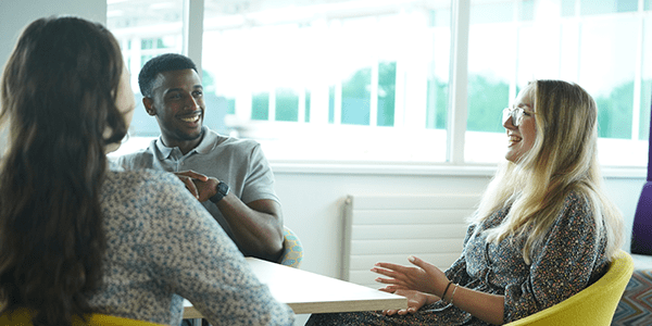 Three colleagues chatting around a table.