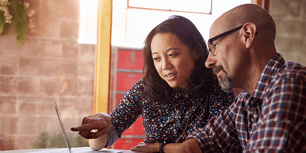 A man and a woman talking whilst looking at a laptop.