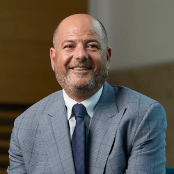 A professional male smiling wearing a grey suit.