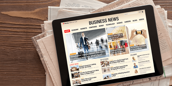 An ipad with business news on it on top of a bunch of newspapers.