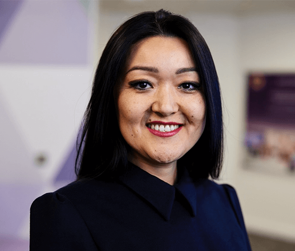 A woman with mid length black hair smiling wearing a navy blue blouse.