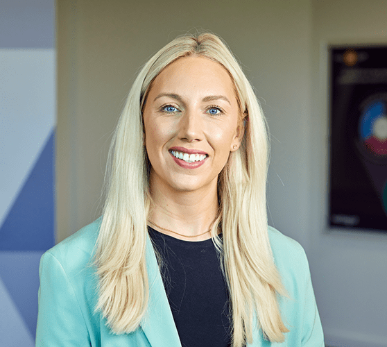 A woman with long blonde hair smiling wearing a blue blazer and black shirt.