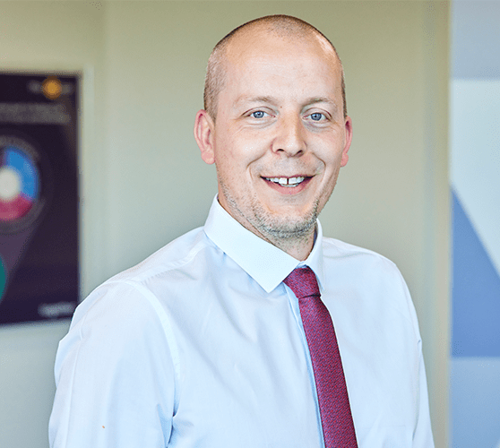 A bald man smiling wearing a white shirt and red tie.