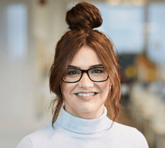 A woman with ginger hair in a bun smiling wearing a white turtleneck.