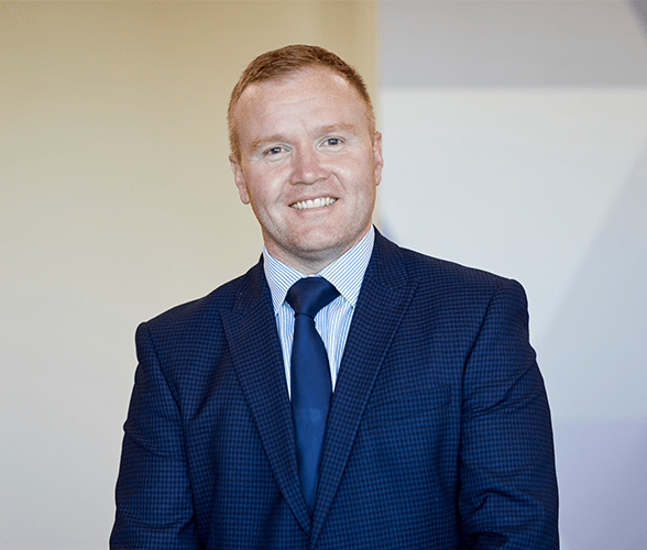 A man with short ginger hair smiling in a blue suit.