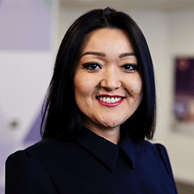 A woman with mid length black hair smiling wearing a navy blue blouse.