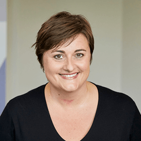 A woman with short brown hair smiling wearing a black blouse.