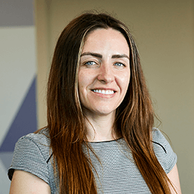 A woman with long brown hair smiling wearing a grey top.