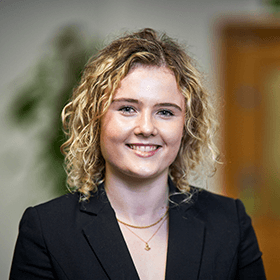 A young woman with short curly hair smiling wearing a black blazer.