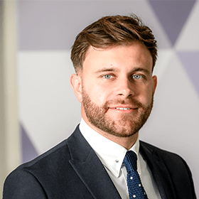 A man with short light brown hair smiling wearing a suit.