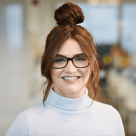 A woman with ginger hair in a bun smiling wearing a white turtleneck.