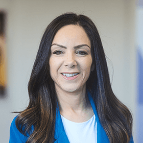 A woman with long brown hair smiling wearing a blue blazer and white shirt.