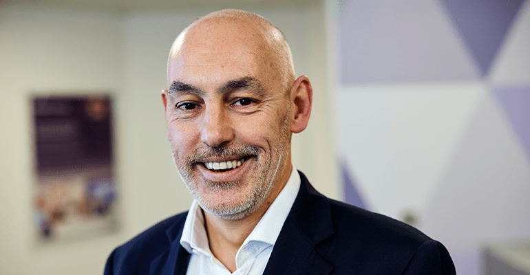 Bald man in blue blazer and white shirt smiling.