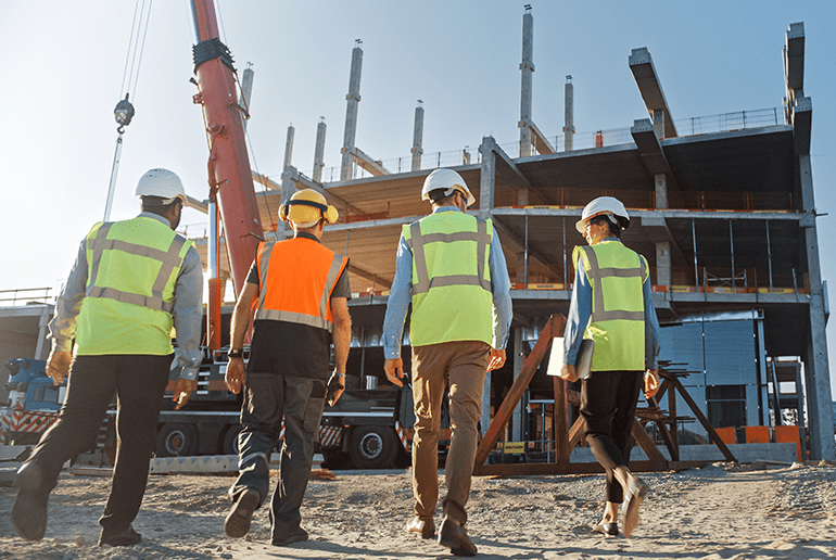 four people in high vis jackets and hard hats walking towards a building development