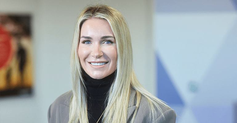 Gemma Roberts wearing a grey blazer and black top smiling.