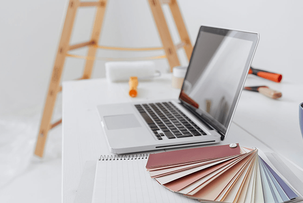 laptop on a desk next to a colour swatch card and a ladder behind the desk