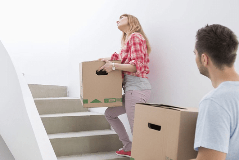 man and woman walking up a staircase carrying brown boxes - l