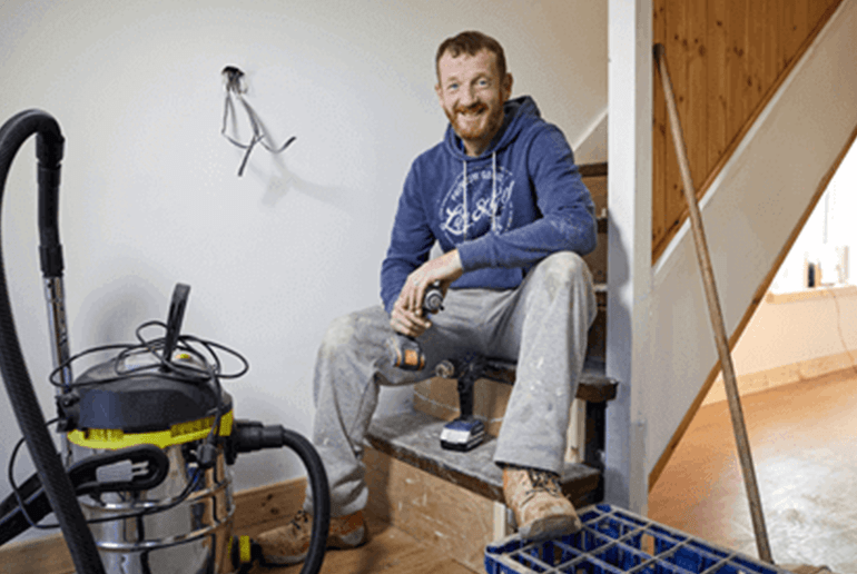 man doing home renovations sat on a staircase holding a drill 