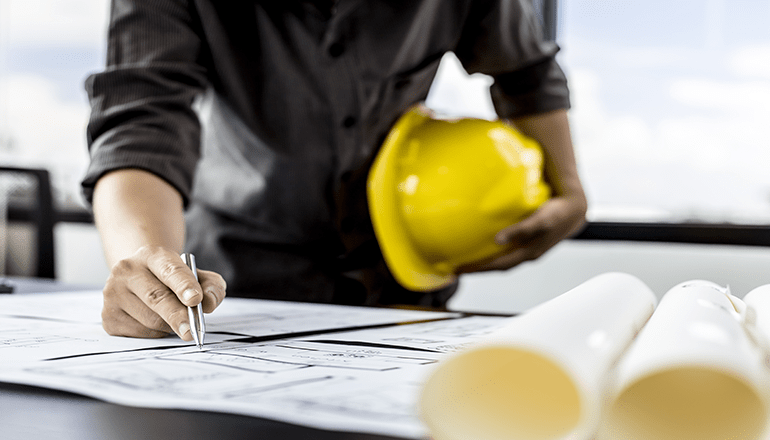 man holding yellow hard hat working on technical drawings