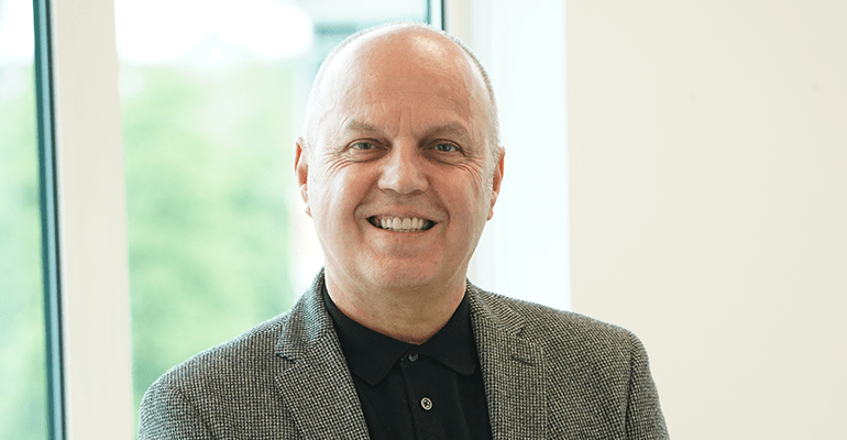 Man in a grey suit smiling.