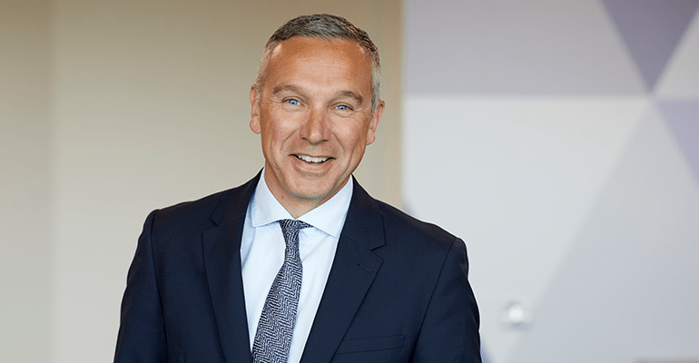 Man in navy suit smiling.