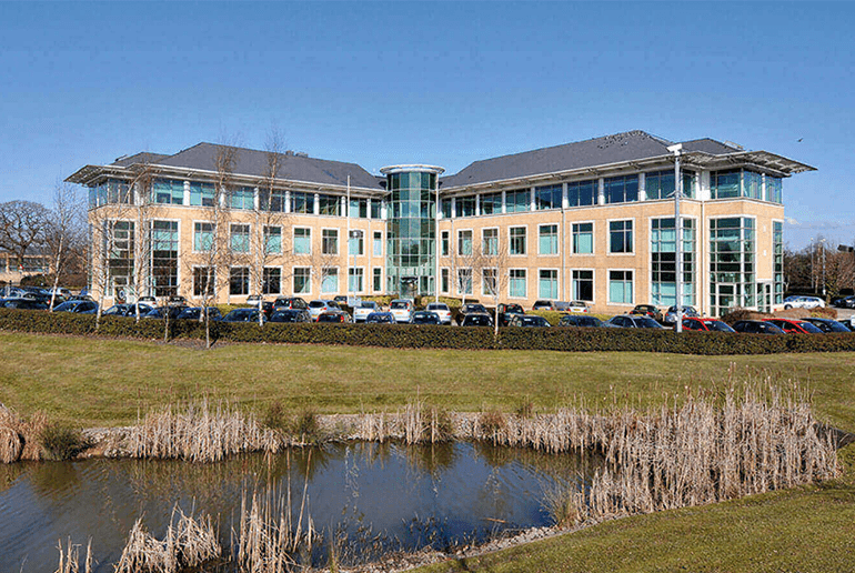 office building with cars parked outside by a lake