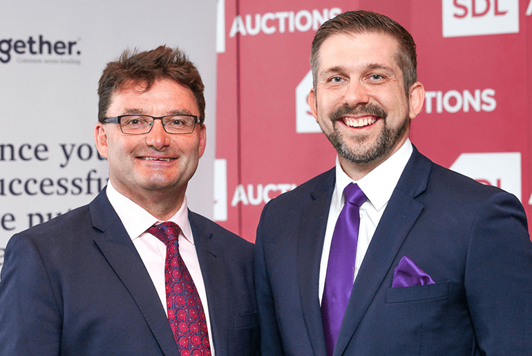 Picture of two men in suits smiling in front of two banners 