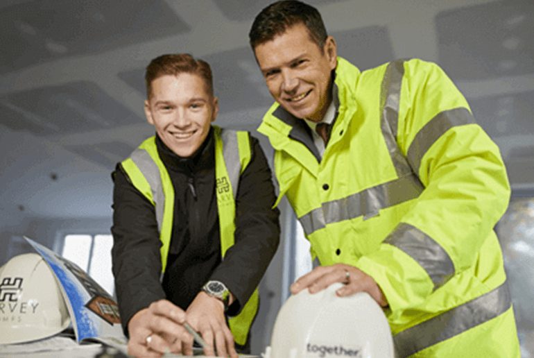 two men wearing high vis jackets stood in front of hard hats