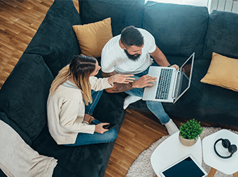 A couple sat on a couch looking at a laptop together.