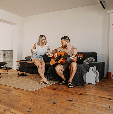 young man and woman sat on a sofa whilst he plays guitar - l