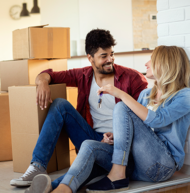 A couple sat on the floor talking with boxes around them.