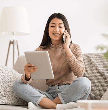 A woman with long brown hair smiling on the phone whilst also on her ipad.