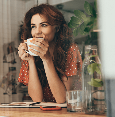 portrait of young woman drinking coffee at table with notebook in cafe - l