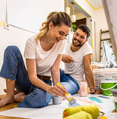 A couple sat on the floor smiling whilst testing paint colours.