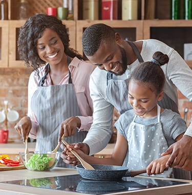 A family of three smiling whilst cooking together.