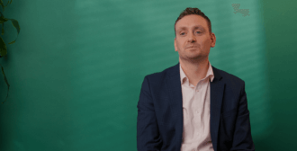 A man sat in front of a green background.