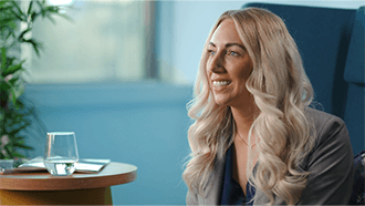 A woman sat on a blue chair with long blonde hair smiling into the distance.