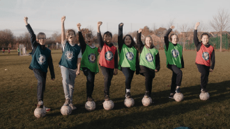 Children standing with one foot on a football and their right arm in the air